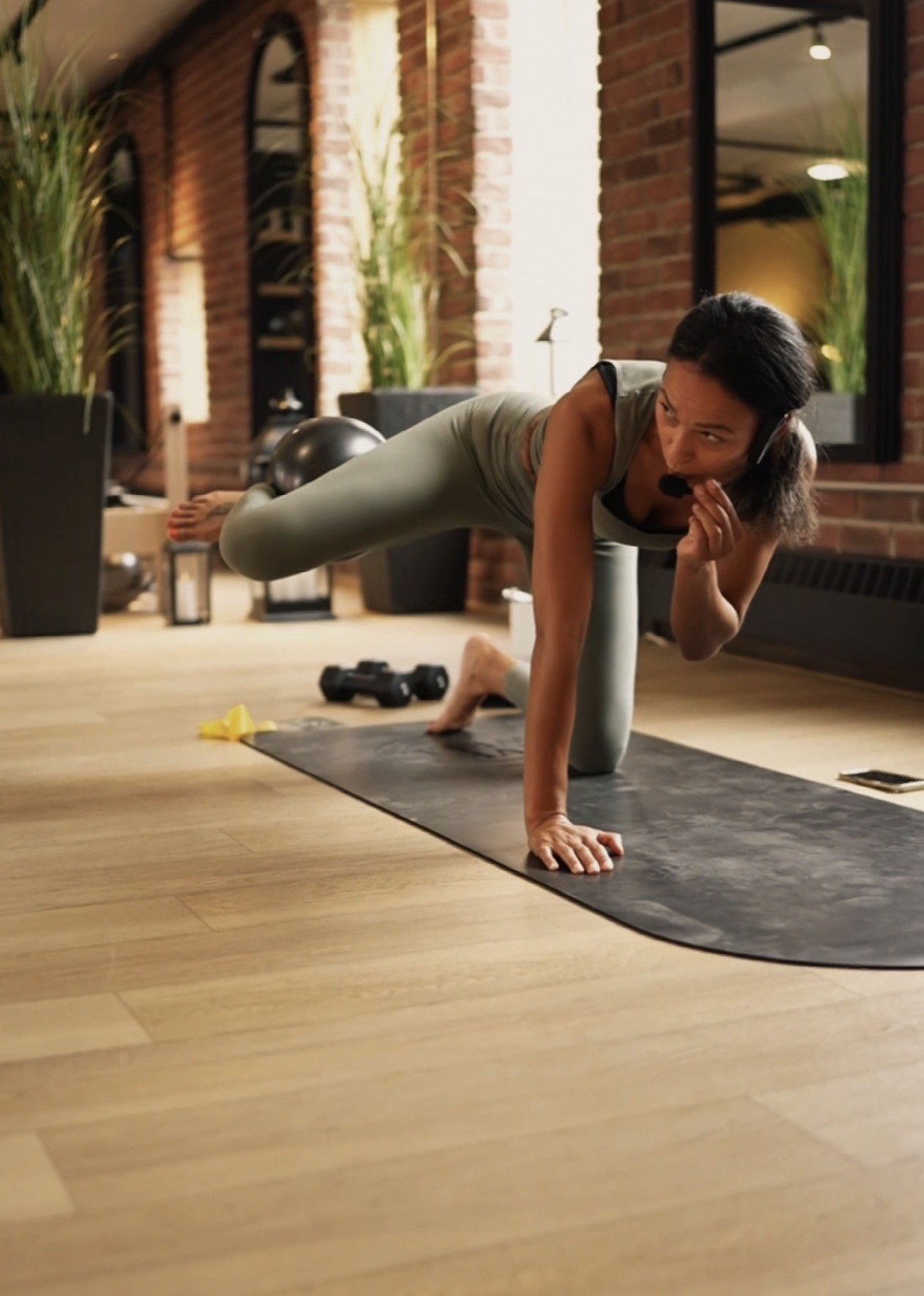 Lara in a green outfit teaching on a mat with a headset microphone