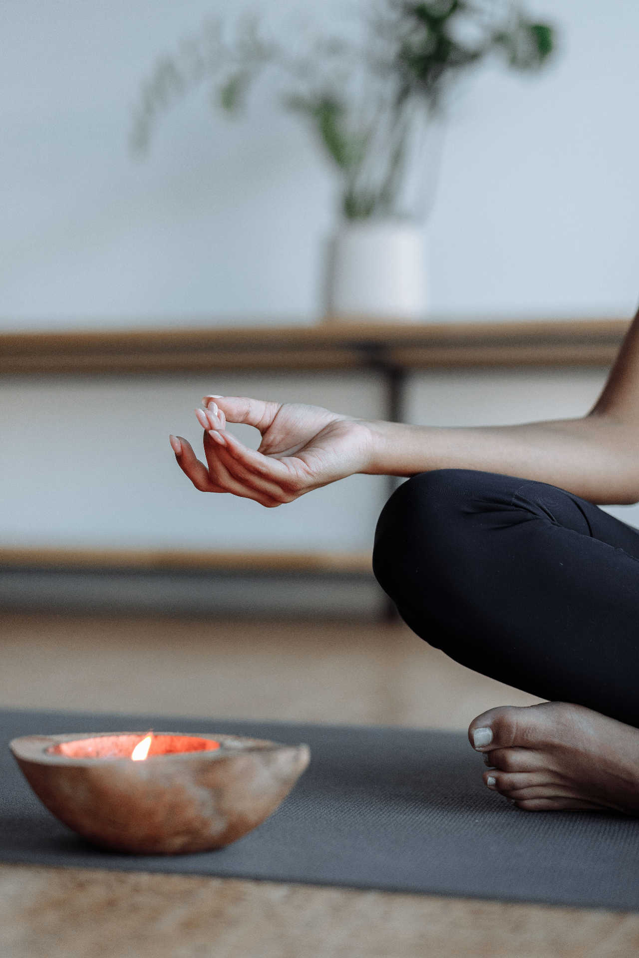 A person seated cross-legged on a yoga mat in meditation with a lit candle in a wooden bowl nearby